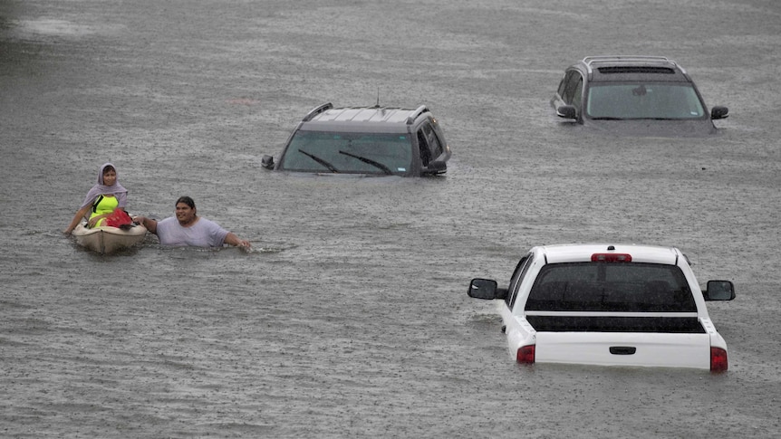 Two people, one in a canoe, make their way through floodwaters that reaches the windscreen on nearby cars.