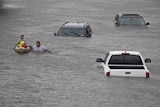 Two people, one in a canoe, make their way through floodwaters that reaches the windscreen on nearby cars.