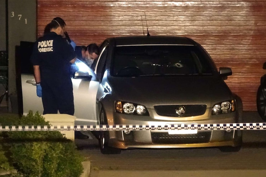 Police forensic officers inspect a car with a bullet hole in the windscreen.