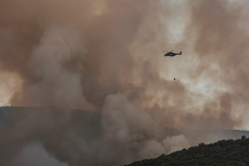 A helicopter flying in front of large clouds of smoke. 