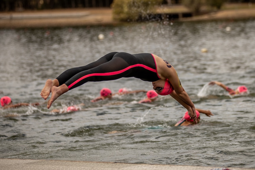 A swimmer in a wetsuit dives into a large body of water.