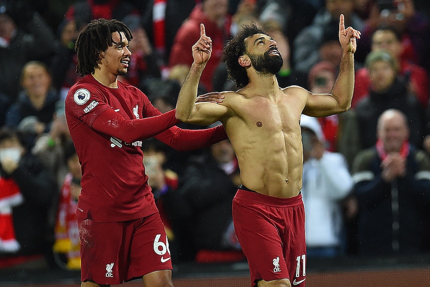 Trent Alexander-Arnold puts his hands on the shoulders of Liverpool teammate Mo Salah, who is shirtless and pointing to the sky.