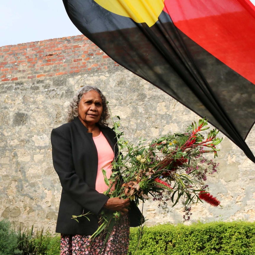 John Pat's aunt Allery Sandy stands in front of an Aboriginal flag at a memorial to her nephew.