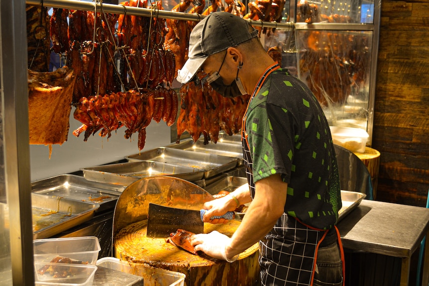 A chef chops meat in a Chinese resturant as cooked ducks hang infront of him