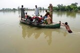 A man pushes a boat with Pakistani flood survivors onboard