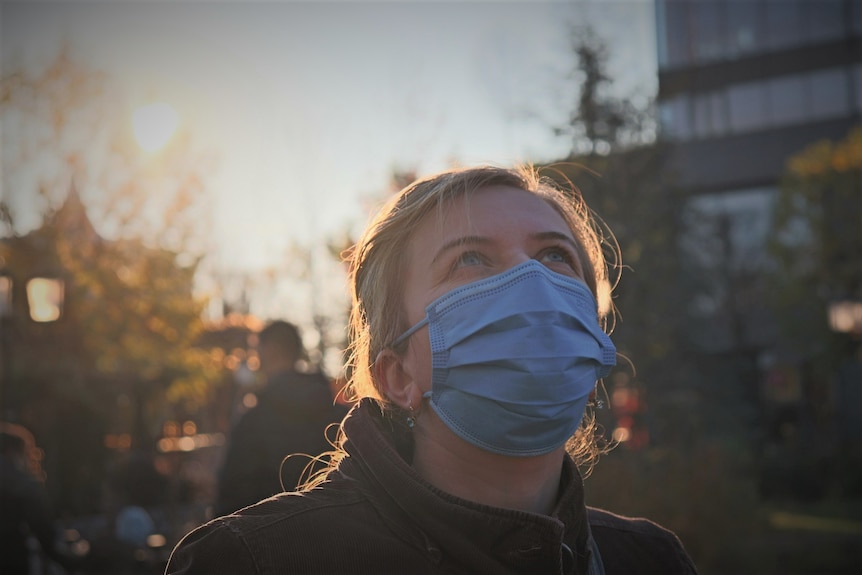 Unidentified female wearing respiratory mask looking upwards while outside.