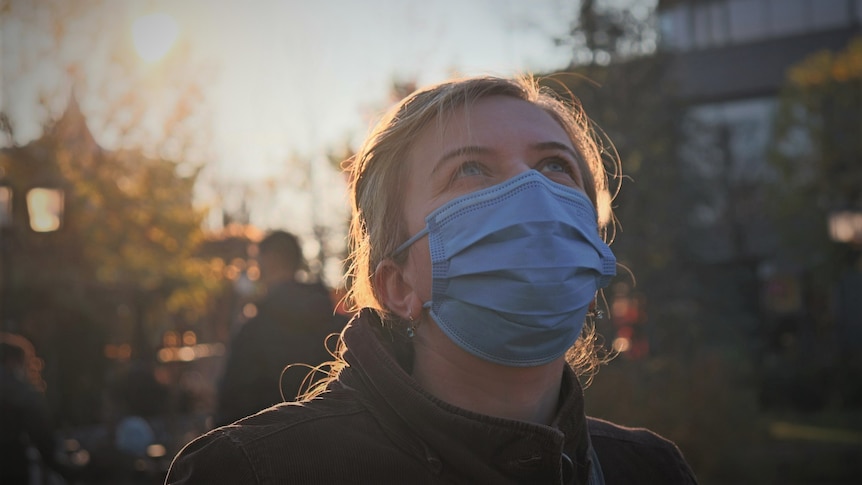 Unidentified female wearing respiratory mask looking upwards while outside.