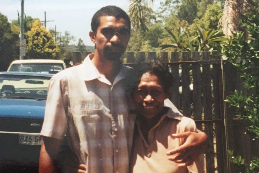 Daniel stands with his arm around his mother in what looks like a backyard.