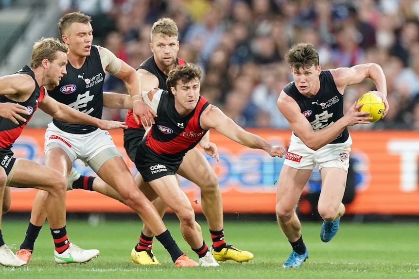 Carlton's Sam Walsh runs away from Essendon players with the ball in hand during their AFL game.