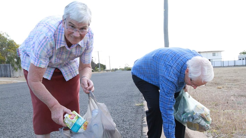 Two elderly women pick up rubbish in the street