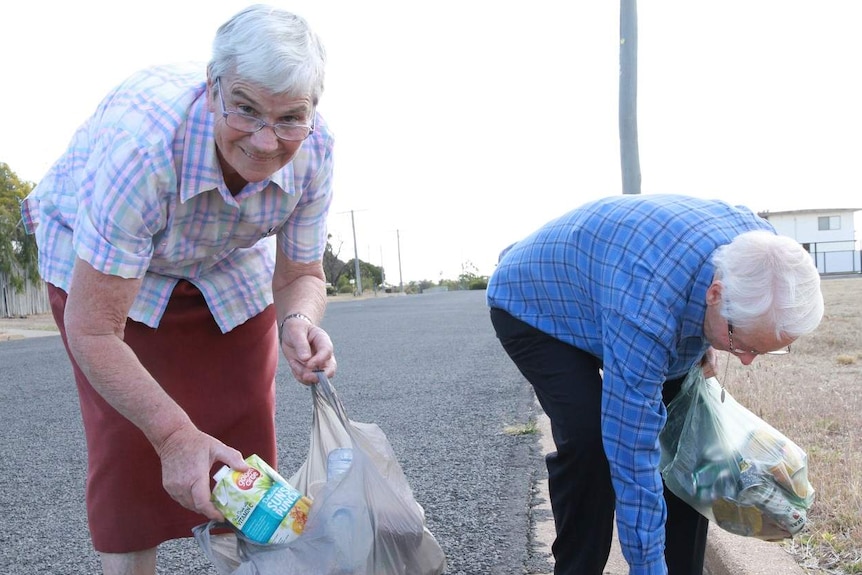 Two elderly women pick up rubbish in the street