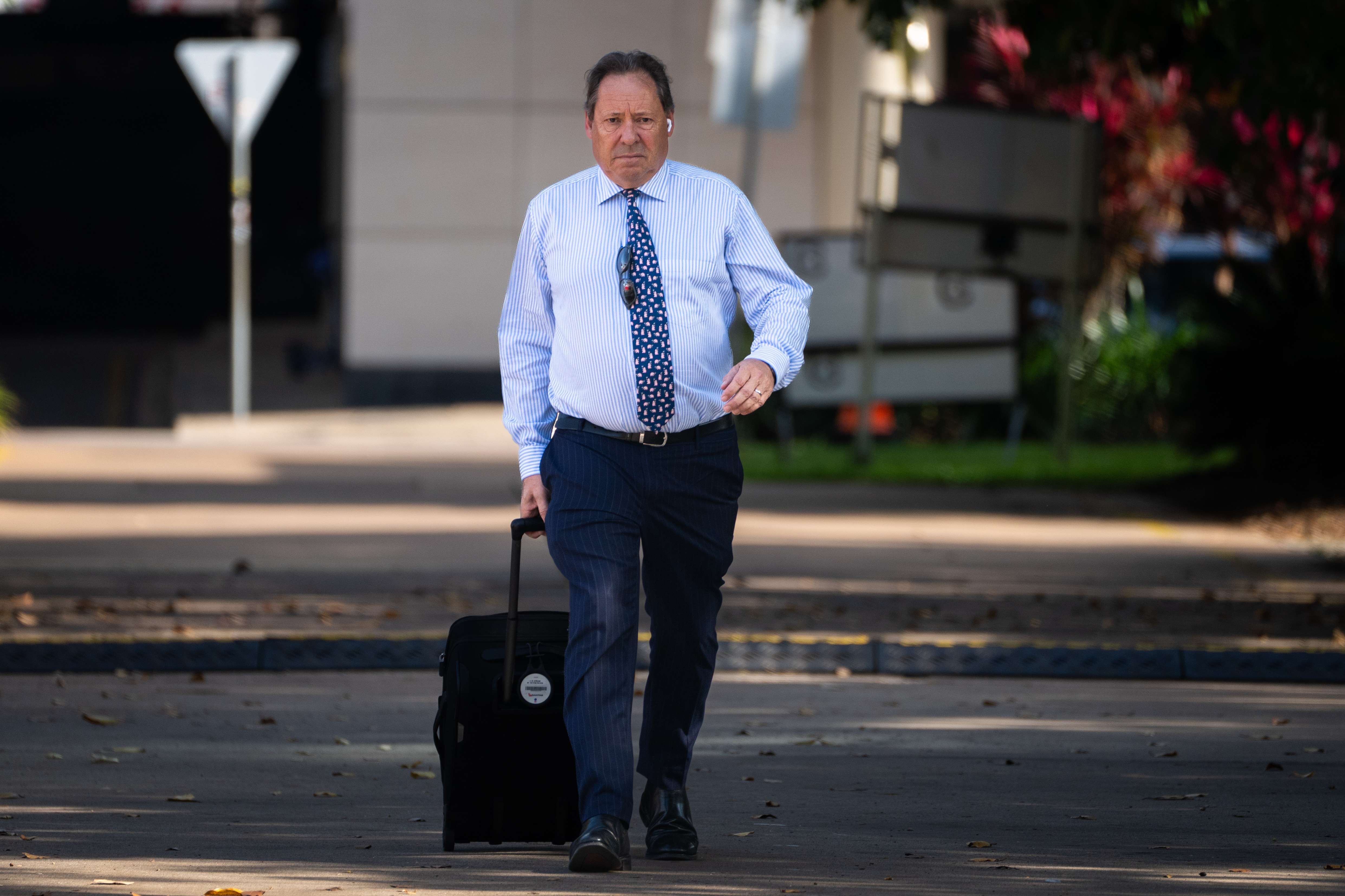 a middle aged man wearing a suit wheeling a suitcase