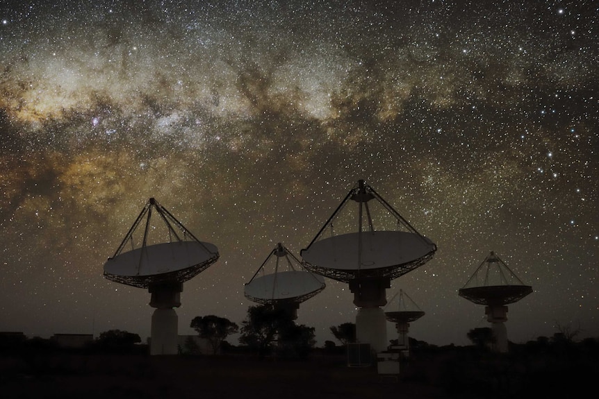 Large satellite dishes point at the night sky, filled with stars.