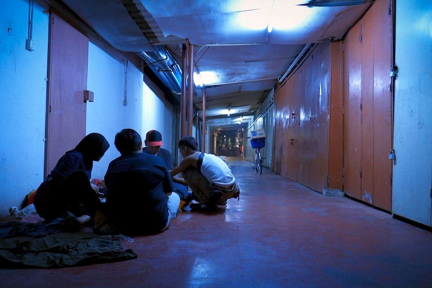 Four people sit on the ground in a closed up market in Kuala Lumpur.