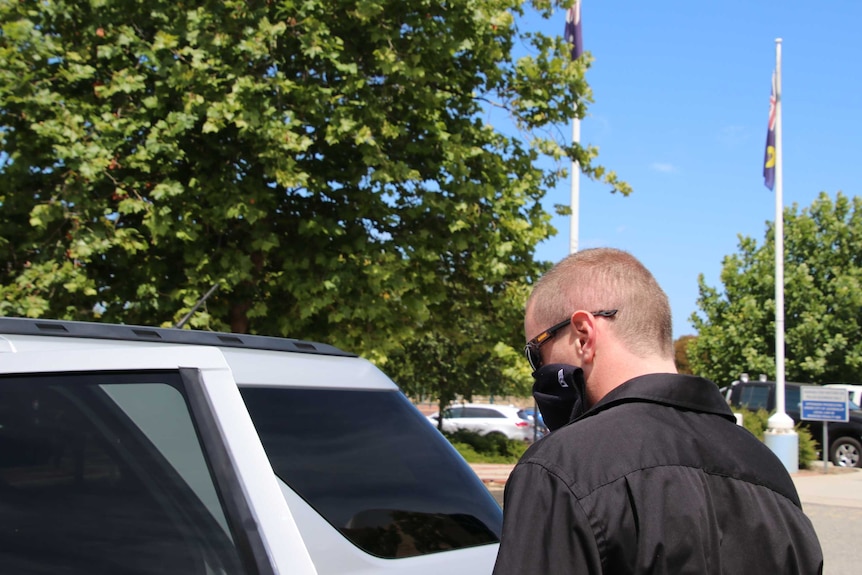 Luke Kevin Dempster with his back to the camera as he leaves court. He is covering his mouth with a baseball cap.