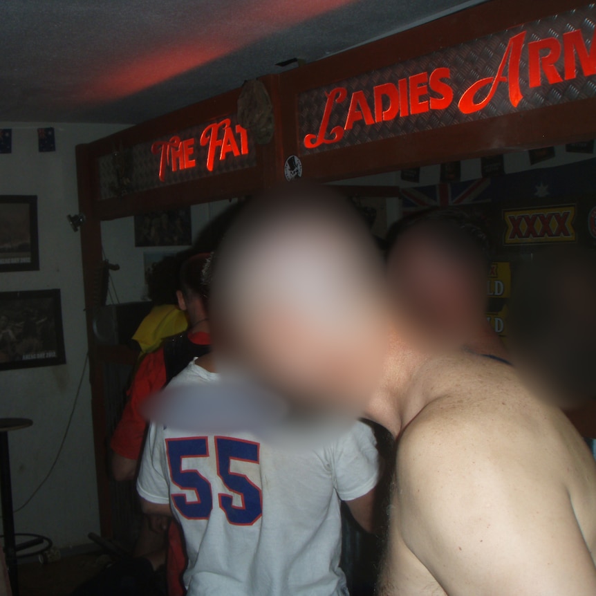A shirtless man and other men stand in front of the bar with The Fat Ladies signage.