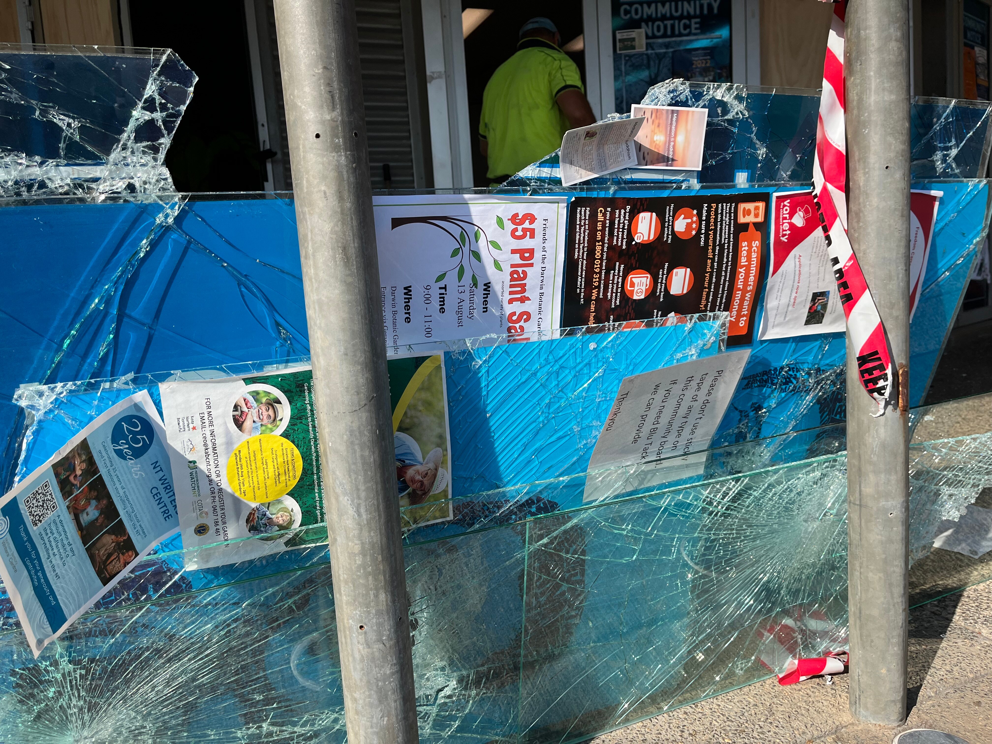 A broken window pane with posters attached to it leans against a metal pole.
