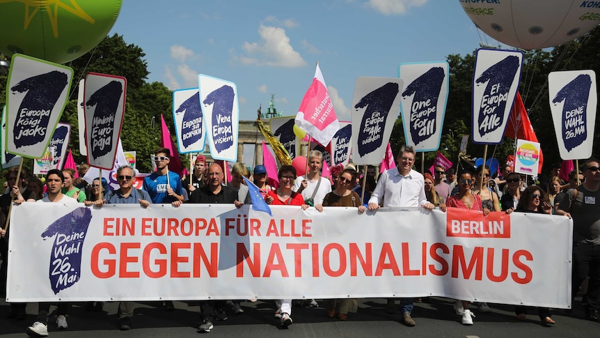 People walk in the street behind a large banner reading 'A Europe for all against nationalism'.
