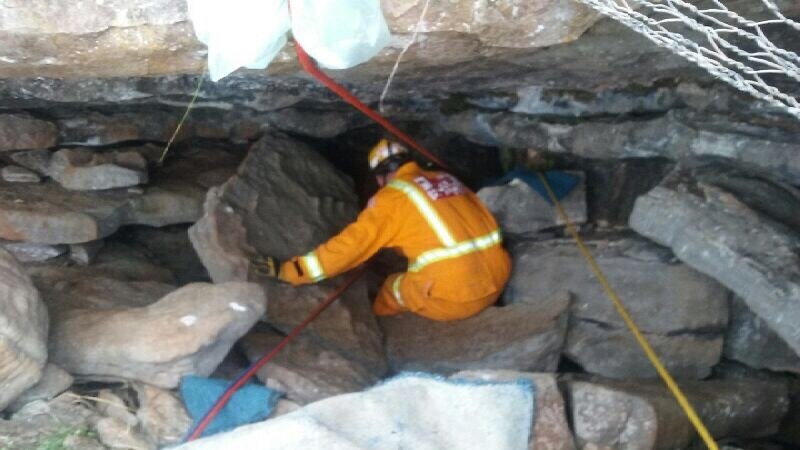 A person in an orange CFA uniform descends into a small cave with the help of ropes.