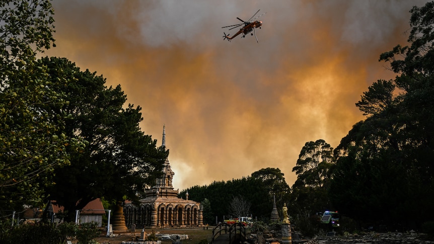 A waterbombing helicopter flies over a monastery.