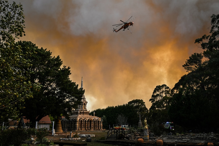 A waterbombing helicopter flies over a monastery.