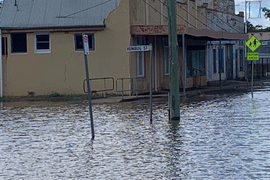 Floodwater covers streets in front of buildings and a streetsign reading "Humbug st".