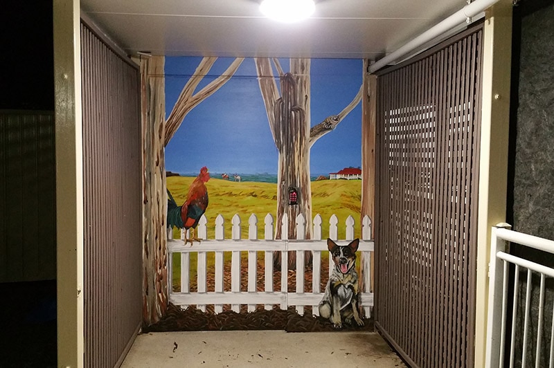 A painted mural depicting a farm with a rooster and a cattle dog.