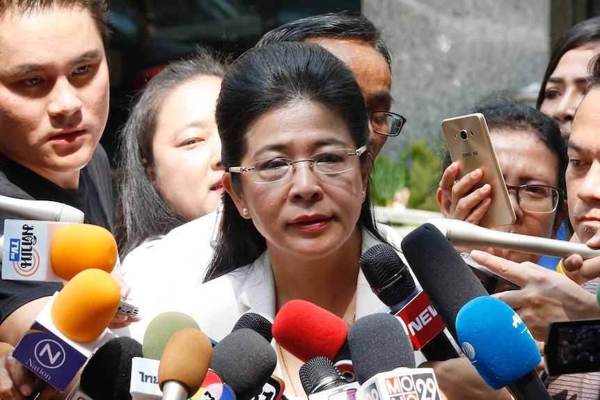 Pheu Thai party leader Sudarat Keyuraphan speaks wearing a white jacket surrounded by microphones and press.