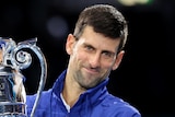 A male tennis player holds a trophy to his right as he poses for photographs