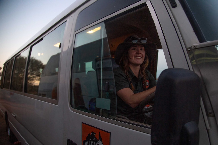 Laura Holmes wears a hat and is behind the wheel of a van. She smiles at the camera.