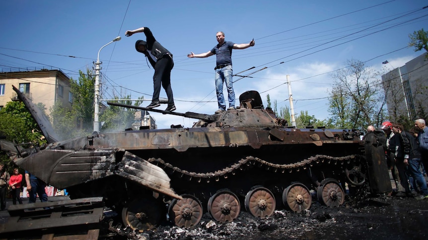 People stand on burnt-out tank in eastern Ukraine