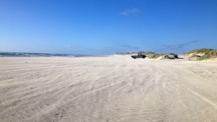 A sandy stretch of Point Moore beach in Geraldton, with a ute parked near sand dunes in the distance.
