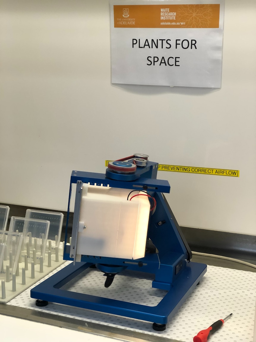 A blue machine with a silver box on a countertop. A sign above reads 'PLANTS FOR SPACE'.