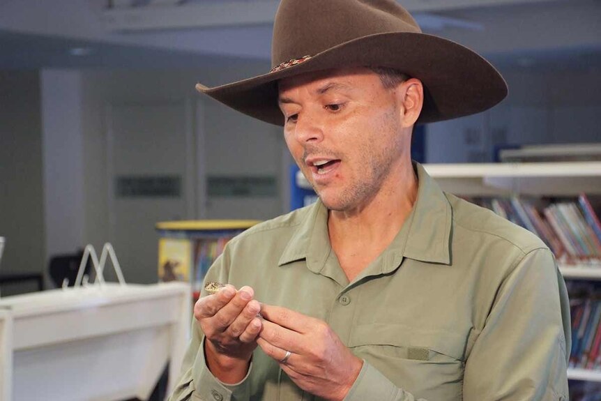 A man in a felt halt hold a lizard.