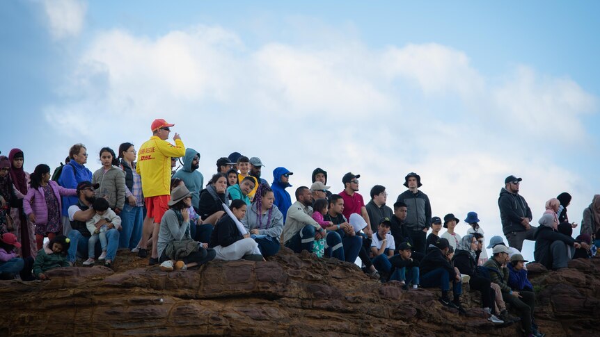 Dozens of anglers and their families watch fishing safety demonstrations from a rock platform.