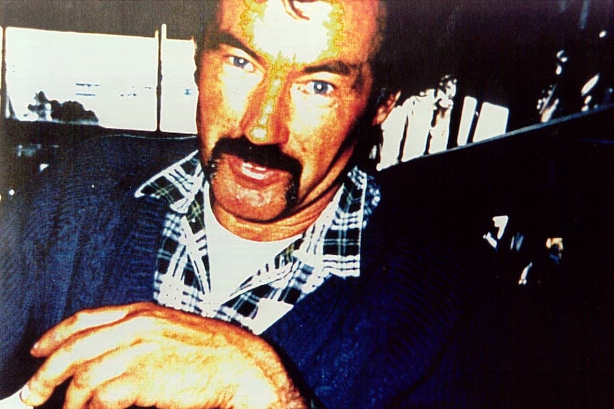 Grainy photo of Ivan Milat wearing a flannelette shirt and blue jumper with a handlebar moustache