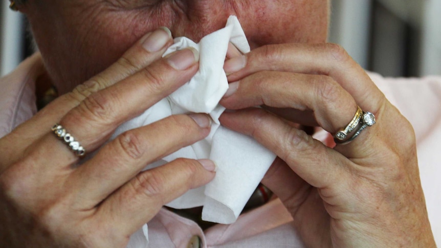 Man holds a tissue to his face to blow his nose.