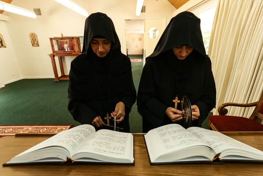 Both nuns with heads bowed in daily prayer.