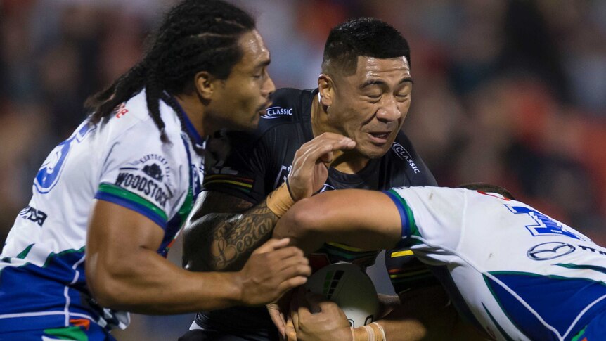 Moses Leota closes his eyes as he gets tackled by two players in white shirts