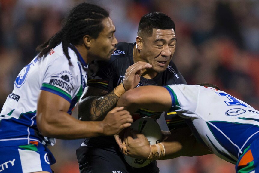 Moses Leota closes his eyes as he gets tackled by two players in white shirts