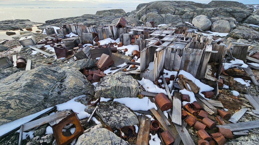 A collection of abandoned wood and rusted barrels partially covered in snow