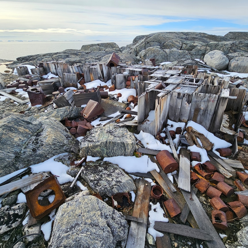 A collection of abandoned wood and rusted barrels partially covered in snow