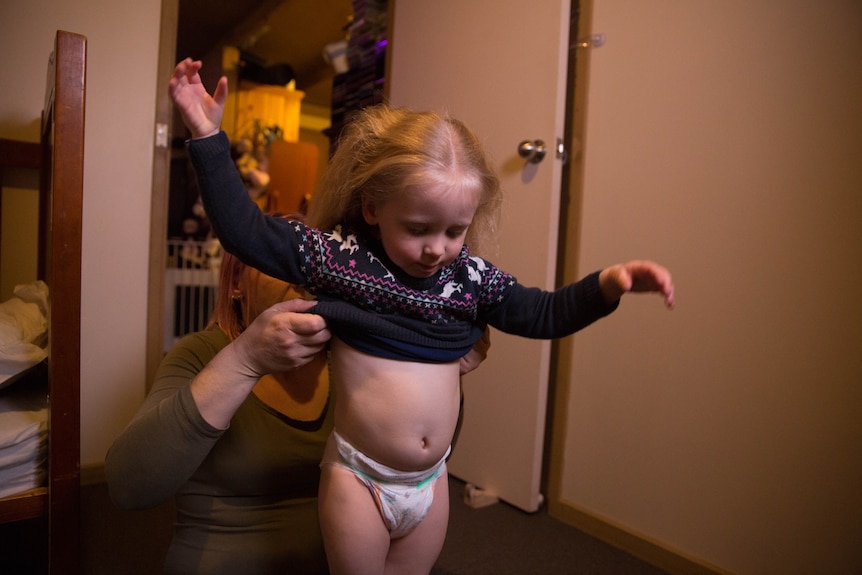 Nara puts her arms up as Amber helps her get dressed.