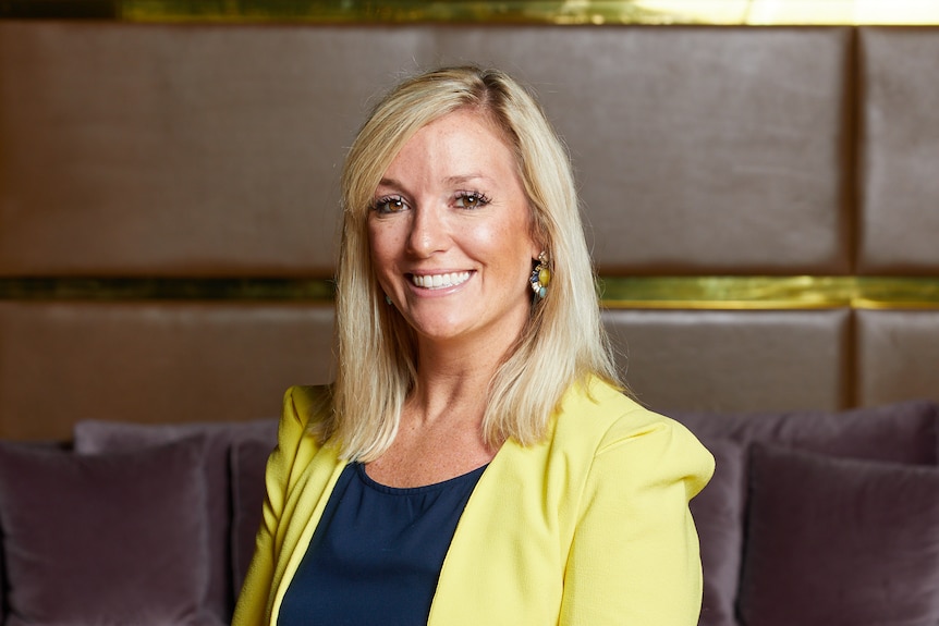 A blonde middle aged woman smiling wearing a yellow blazer with a black top smiling