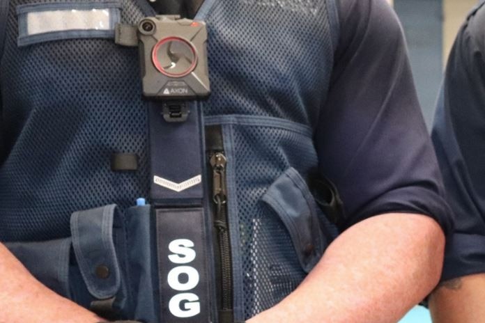 A NSW Correctional Officer wearing gloves stands with his hands clasped at his front.