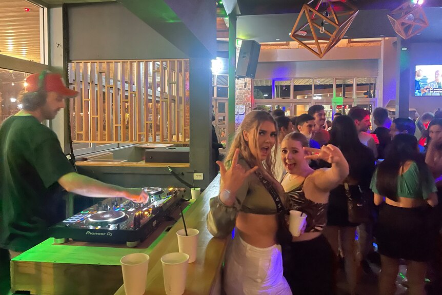 two woman pose infront of DJ  
