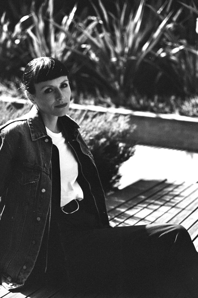 A black and white image of a woman sitting outside on a concrete ledge, slightly reclining.