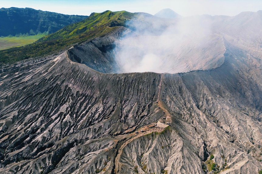 A volcano with smoke coming out of it and hills in the background.