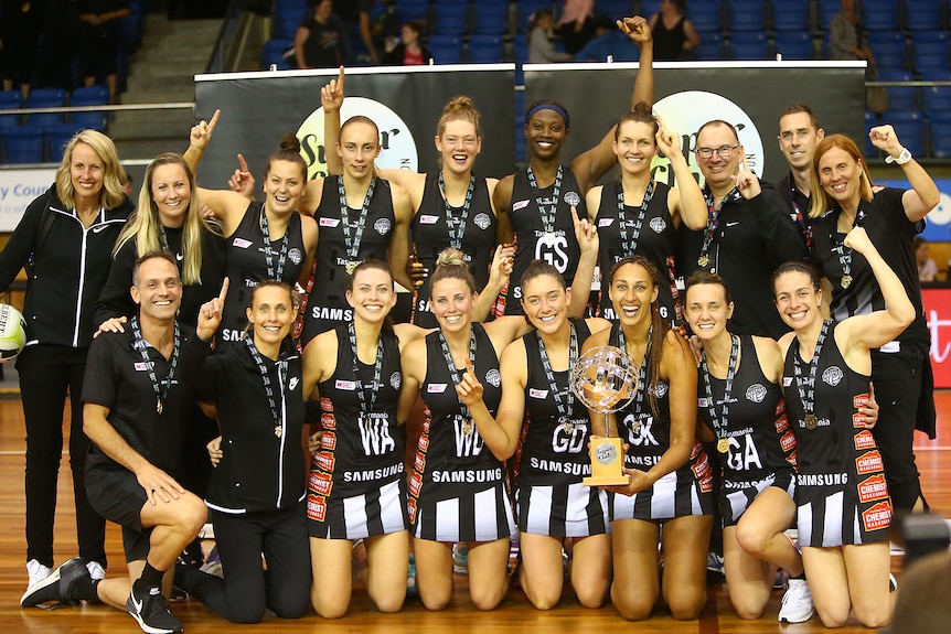Collingwood netball players pose with the trophy and their medals