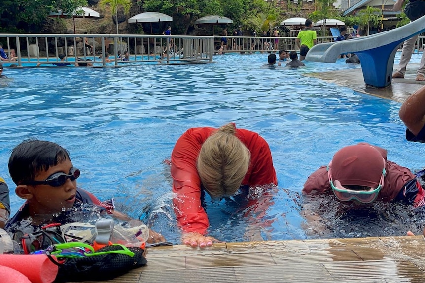 A woman teaching kids to swim in the pool.